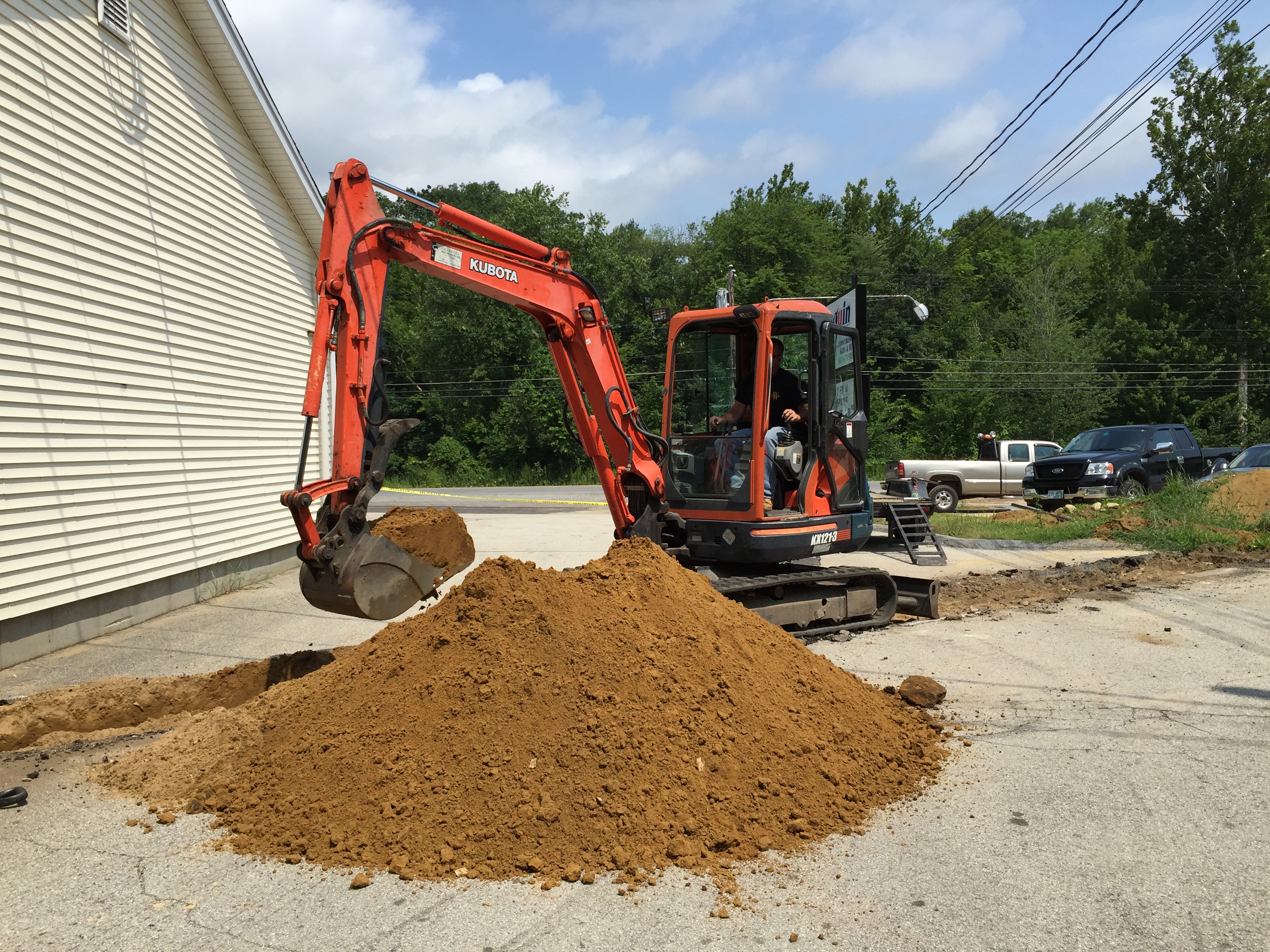 Kubota excavator digging beside commercial building
