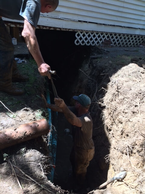 Workers installing sewer pipe in deep trench