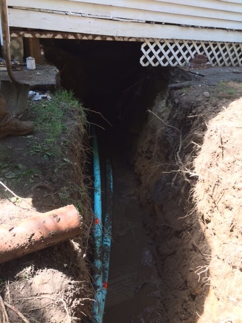 Open trench with new sewer pipe alongside house