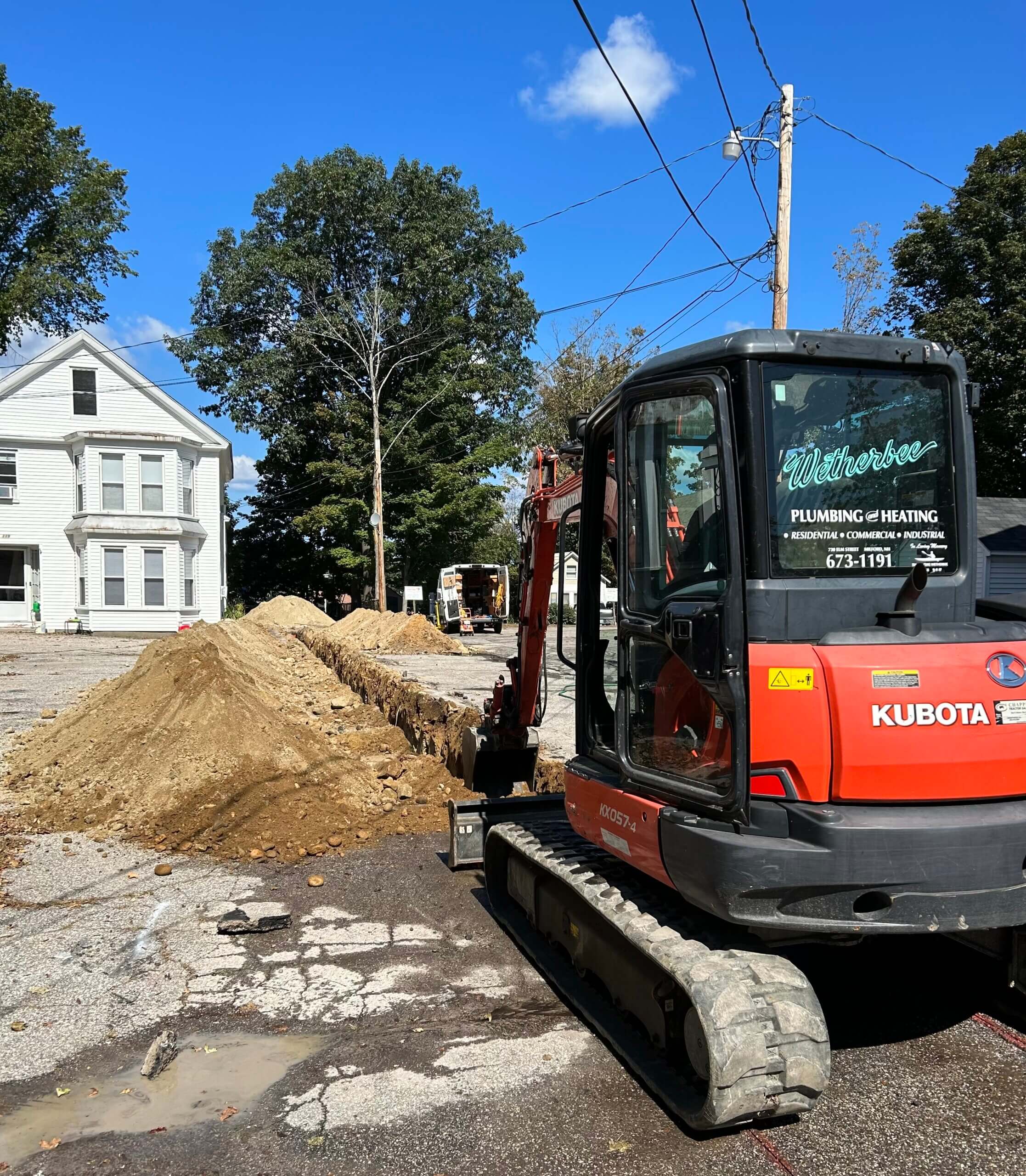 Excavator digging sewer trench along residential street